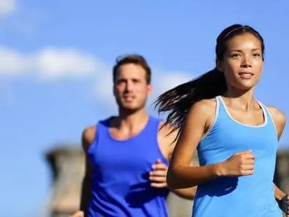 A man and a woman in blue athletic tops jogging outdoors under a blue sky