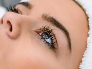 A woman lying back as a gloved clinician injects near her upper lip with a syringe