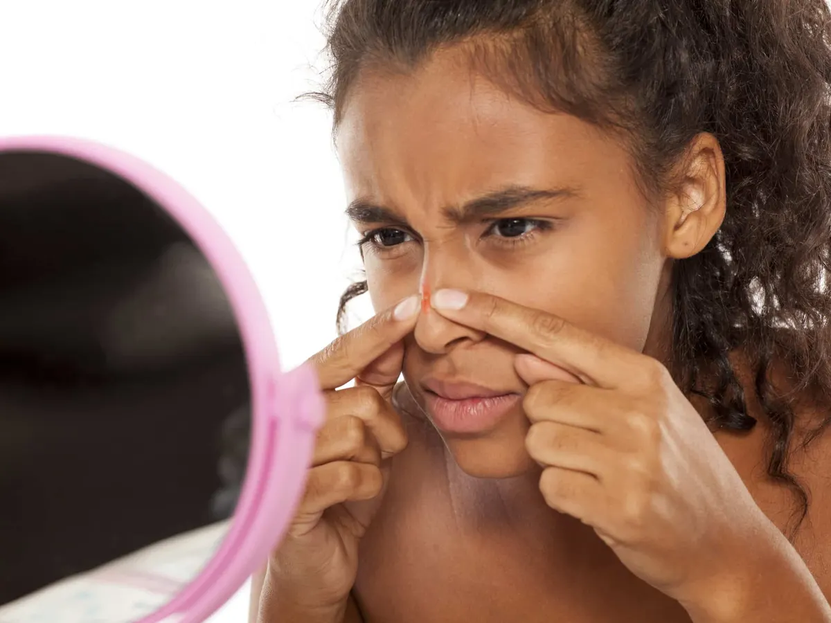 A woman looking in the mirror at a blemish on her nose.