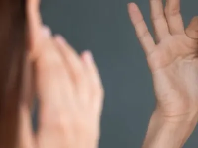 A woman looking into a mirror while touching her forehead and temple with both hands