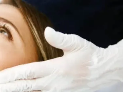 A woman with her face tilted up as a clinician in white gloves holds her face during a skin treatment