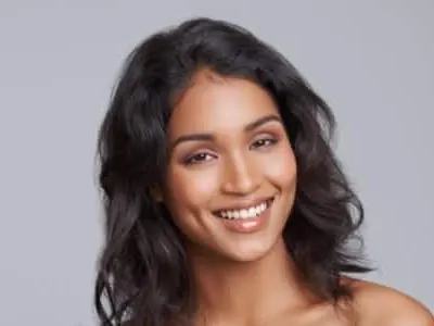 A smiling woman with long dark wavy hair and bare shoulders against a gray background