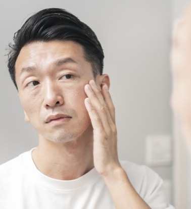 A man touching his cheek while checking his skin