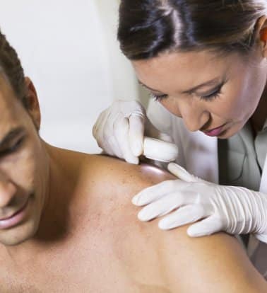 A dermatologist in gloves examining a mole on a man's shoulder