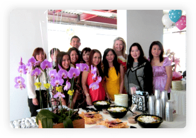 A group of staff members smiling together at an office celebration with orchids and food