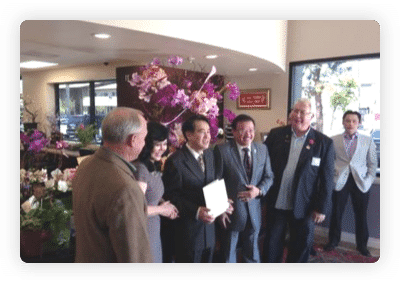 Guests in suits gathered among orchid arrangements at an office opening event