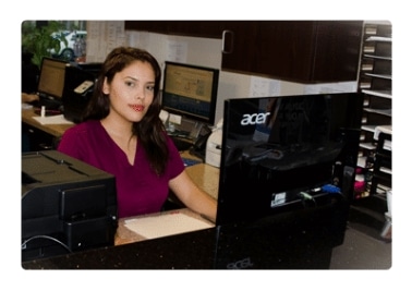 A front desk staff member in scrubs seated at the reception computer
