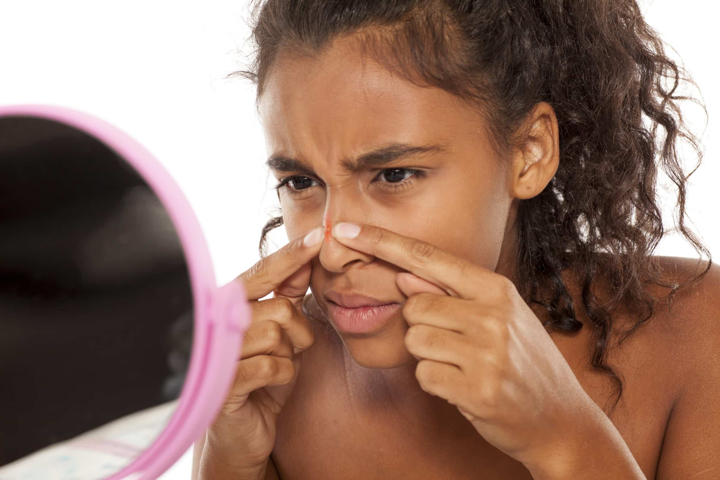 A woman looking in the mirror at a blemish on her nose.