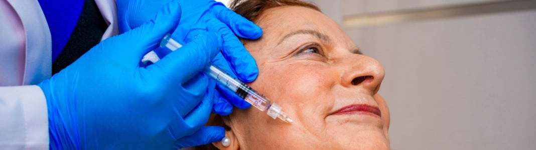 An older woman receiving a facial injection at the cheek from a clinician in blue gloves