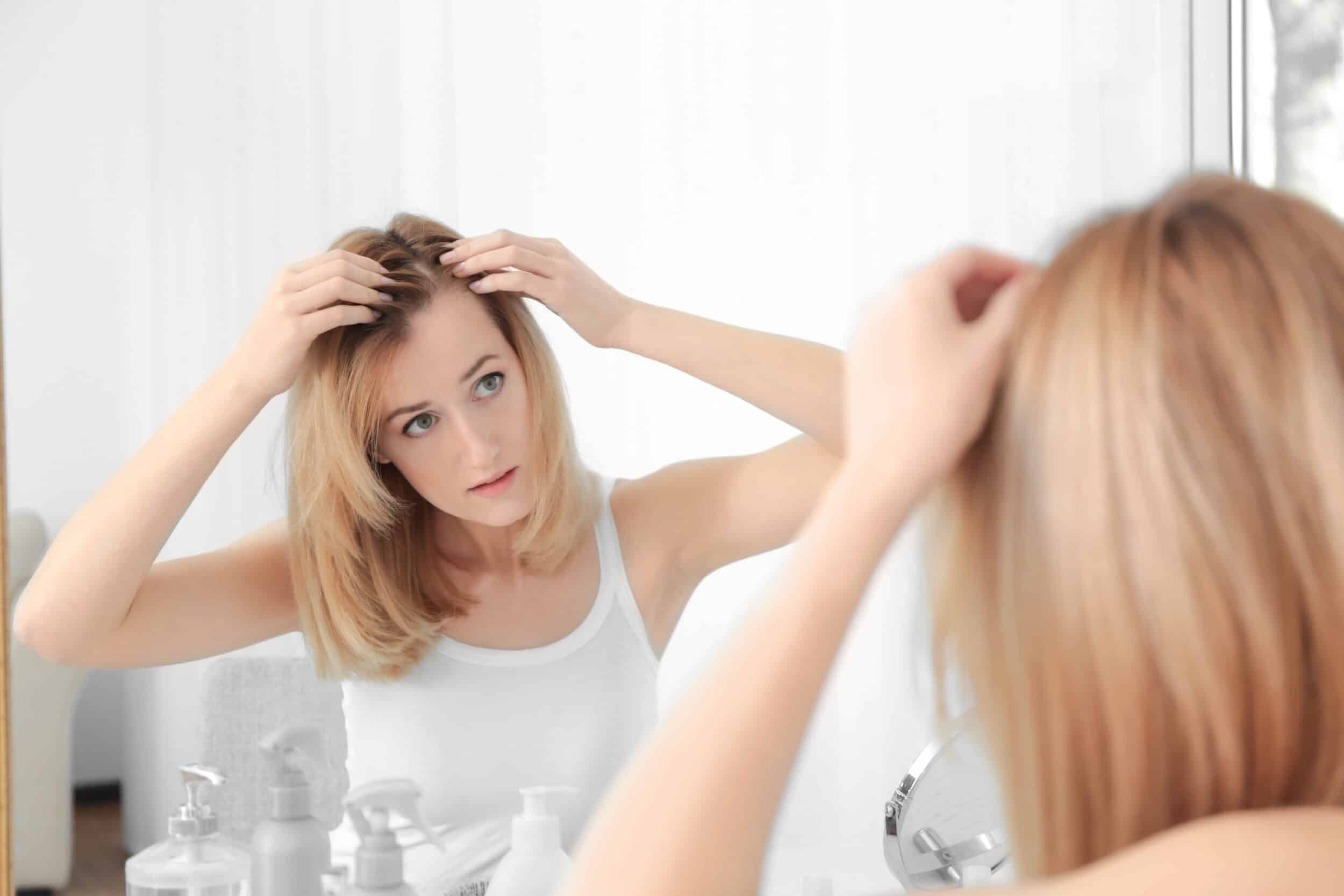 Woman in her 30s looking at hair and scalp in mirror, experiencing hair loss